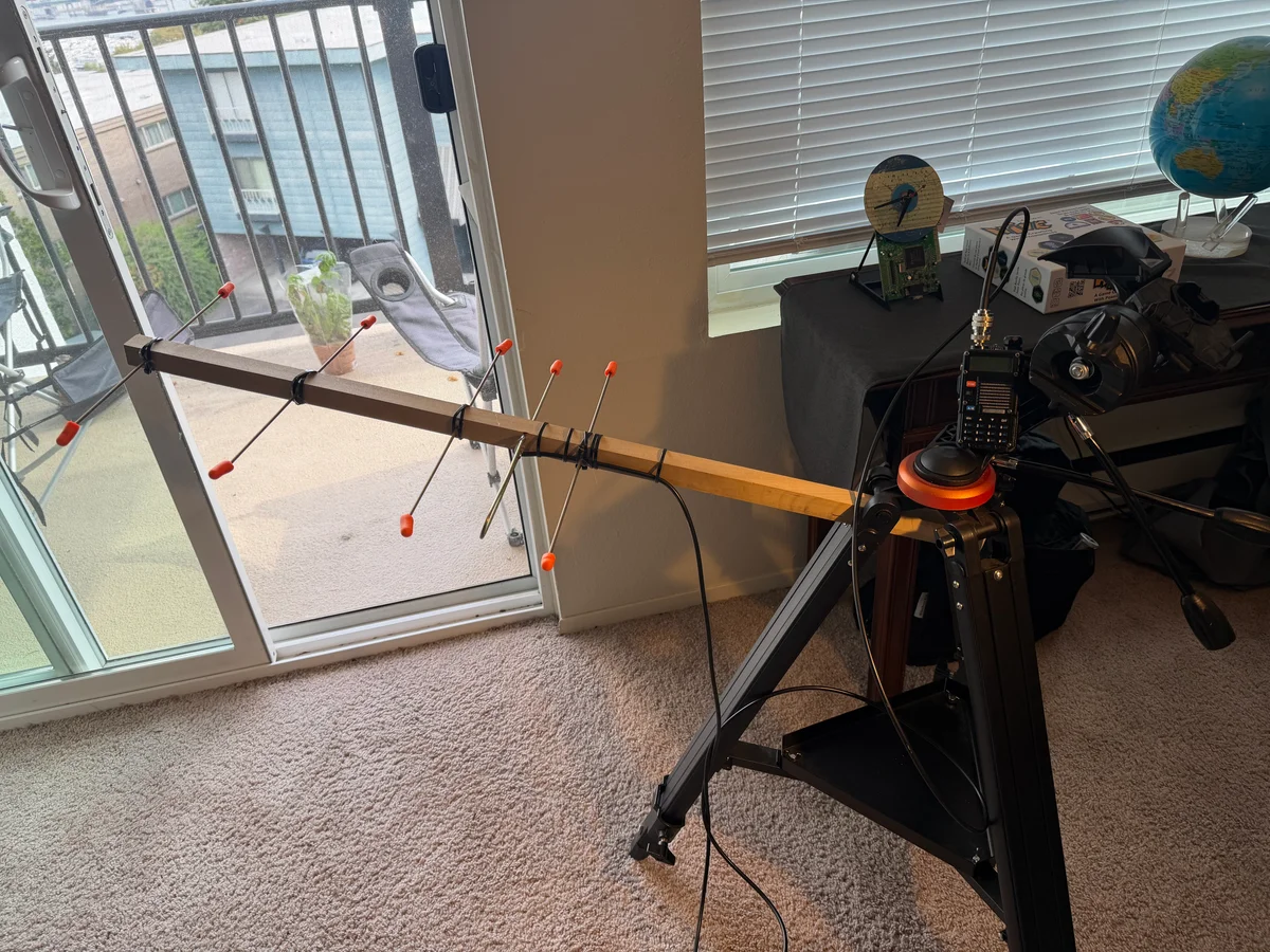 Homemade Yagi antenna with metal elements attached to a wooden boom, mounted on a tripod beside a window